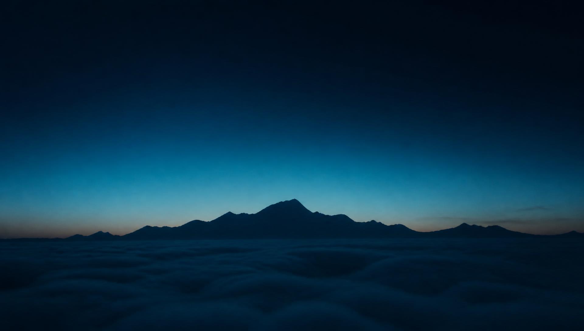 Distant mountain silhouette rising above a sea of clouds at twilight